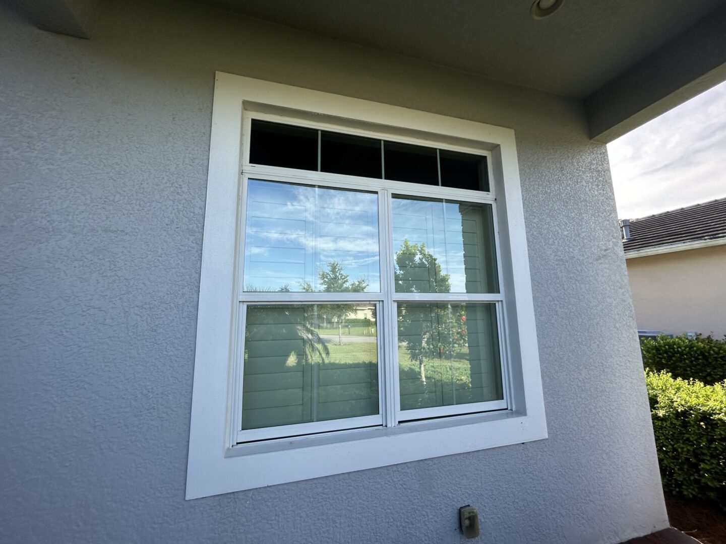 A white-framed window on a stucco building reflects trees and sky.